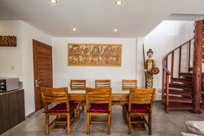 A dining area with a wooden table and chairs, a large decorative painting, and a staircase. - 5 Star Villa for Rent in Bali, Bali Villa 2068 (Bali)