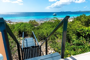 Un escalier menant à une plage où se trouve un bateau à flot, avec une vue sur l’océan.