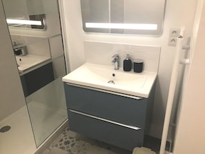 Une salle de bain moderne avec un lavabo blanc, deux tiroirs, un miroir et une cabine de douche en verre.