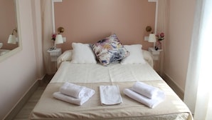 A neatly made bed with white linens and a floral pillow, two bedside tables with lamps, and a mirror on the wall. - Hostal Emperador (Merida)