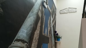 A hallway with a large mural, a marble column, and a potted plant. - Hostal Emperador (Merida)