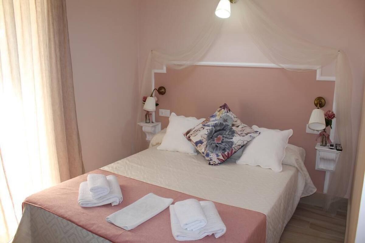 A neatly made bed with white linens and a pink bedspread, two bedside lamps, and a floral pillow.