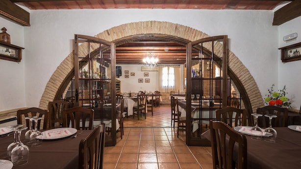 Un comedor con un arco de ladrillo, mesas de madera, sillas y suelo de baldosas.