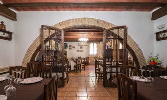 Un comedor con un arco de ladrillo, mesas de madera, sillas y suelo de baldosas.