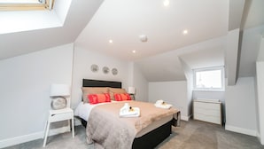 Een moderne slaapkamer met een groot bed, nachtkastje, raam en plafondlamp.
