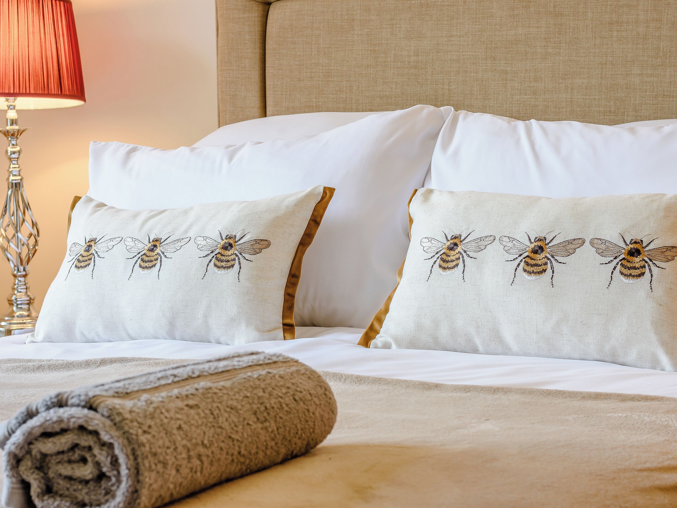 A neatly made bed with white pillows and a rolled towel.
