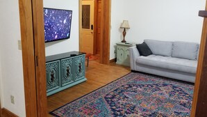 A living room with a television, a light-colored sofa, a patterned rug, a cabinet, and a door.
