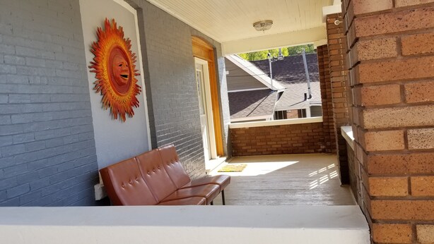 A covered outdoor seating area with a bench and a wall-mounted sun decoration.