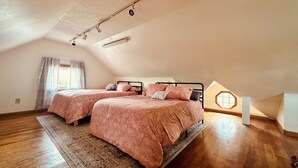A bedroom with two beds, a wooden floor, a large rug, and a skylight.