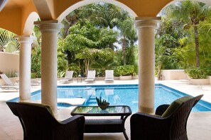 Un espace piscine agrémenté de chaises longues et d’une table, entouré de colonnes et de plantes tropicales.