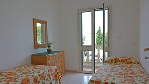 Een slaapkamer met twee bedden, een dressoir, een spiegel en een schuifpui naar een buitenruimte.