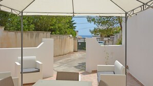 Een overdekt terras met witte rieten meubels en uitzicht op zee.