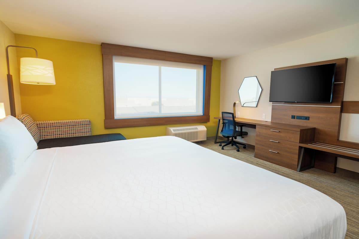 Une chambre d’hôtel avec un grand lit, un bureau avec une chaise, un téléviseur à écran plat et une fenêtre avec des stores.