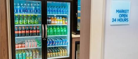 A vending machine with a variety of beverages and snacks, and a sign indicating the market is open 24 hours.
