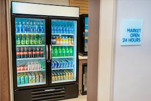 Een automaat met diverse dranken en snacks, en een bord dat aangeeft dat de markt 24 uur per dag geopend is.