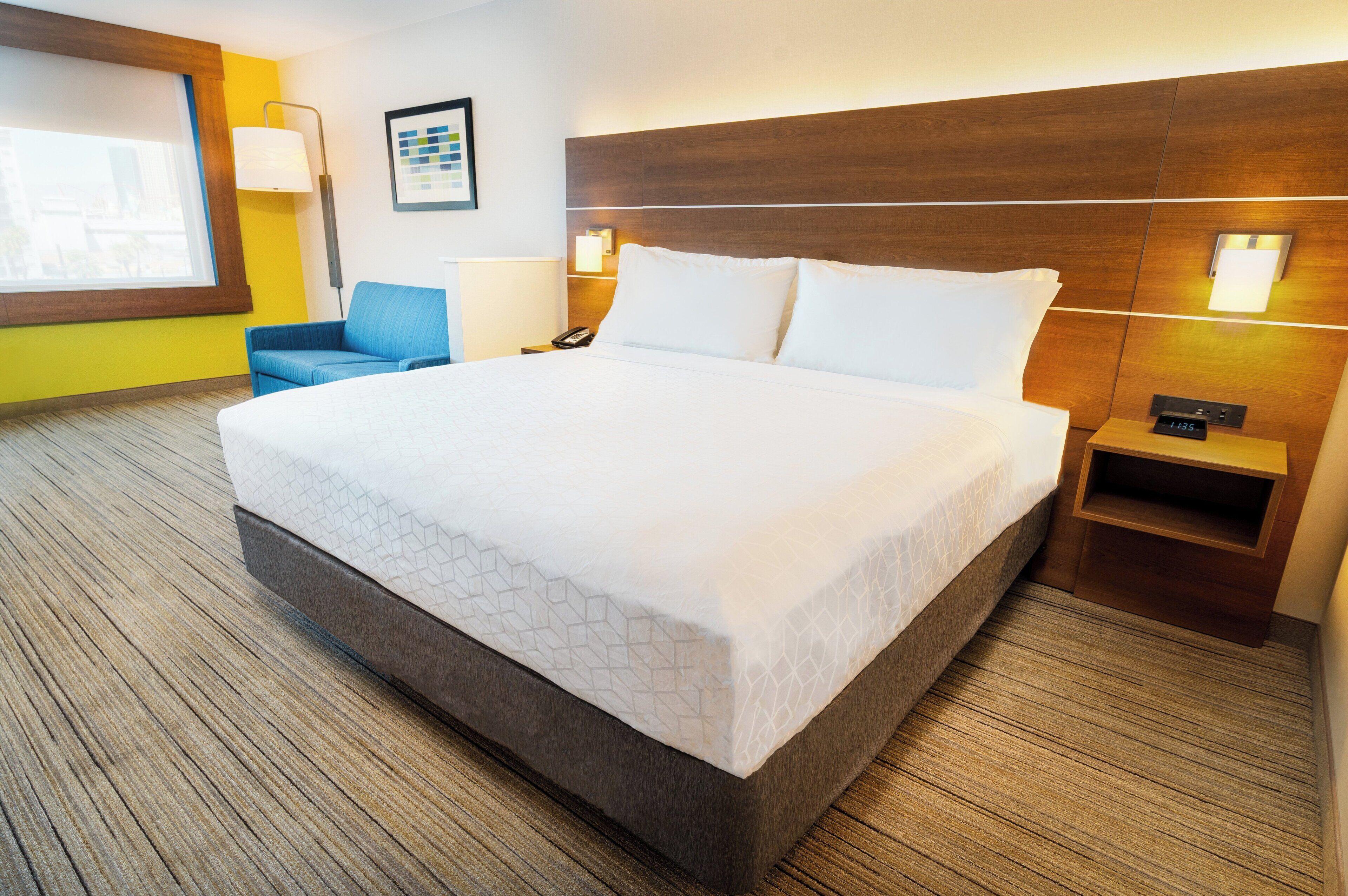 A hotel room with a large bed, a nightstand, a lamp, and a chair.