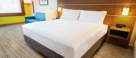 A hotel room with a large bed, a nightstand, a lamp, and a chair.