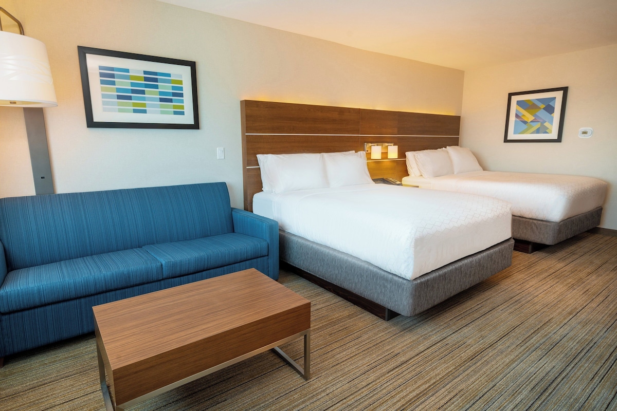 Een hotelkamer met een blauwe bank, een houten salontafel, een bed met wit beddengoed en twee nachtkastjes met lampen.