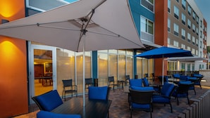 An outdoor patio with tables and chairs, large umbrellas, and a glass door entrance.