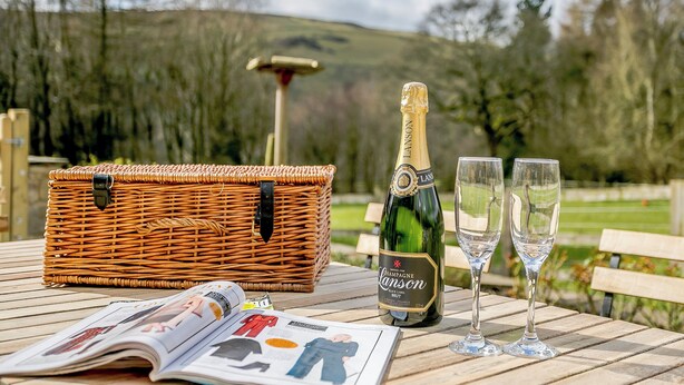 A wicker basket, a bottle of champagne, and two glasses on a table with a magazine. - 3 bedroom accommodation in Hathersage (Hathersage)