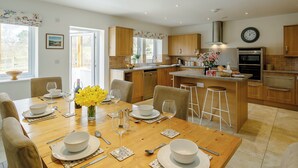 A modern kitchen with wooden cabinets, a central island, and a dining area with a table set for four. - 3 bedroom accommodation in Hathersage (Hathersage)
