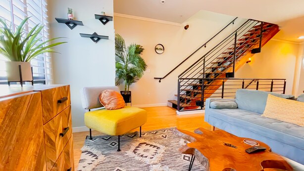 Een moderne woonkamer met een houten kast, een gele stoel, een blauwe bank, een houten salontafel en een trap.