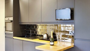 A modern kitchen with grey cabinets, a stainless steel stove, a tiled backsplash, and a wooden countertop.