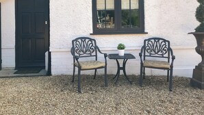 An outdoor seating area with two chairs and a small table, a window with blinds, and a door.