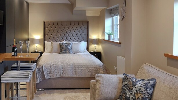 A modern bedroom with a large bed, bedside tables, a sofa, and a small table with a bottle and glasses.