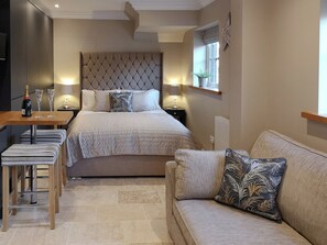 A modern bedroom with a large bed, bedside tables, a sofa, and a small table with a bottle and glasses. - The White House Studio (Worthing)
