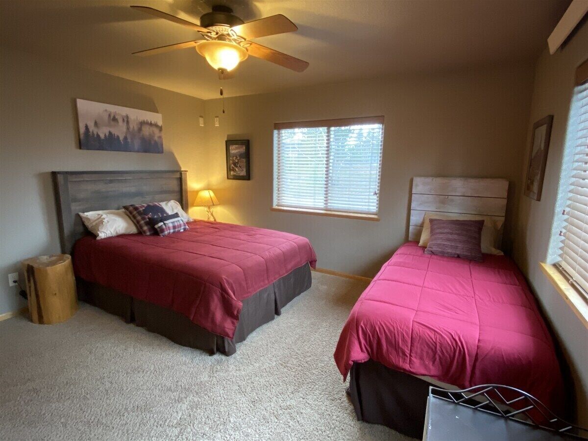 A bedroom with two beds, a ceiling fan, a window with blinds, and a lamp.