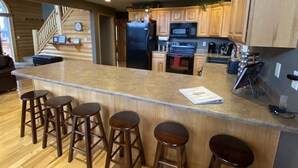 A kitchen with wooden cabinets, a central island with stools, a refrigerator, microwave, oven, and a coffee machine.