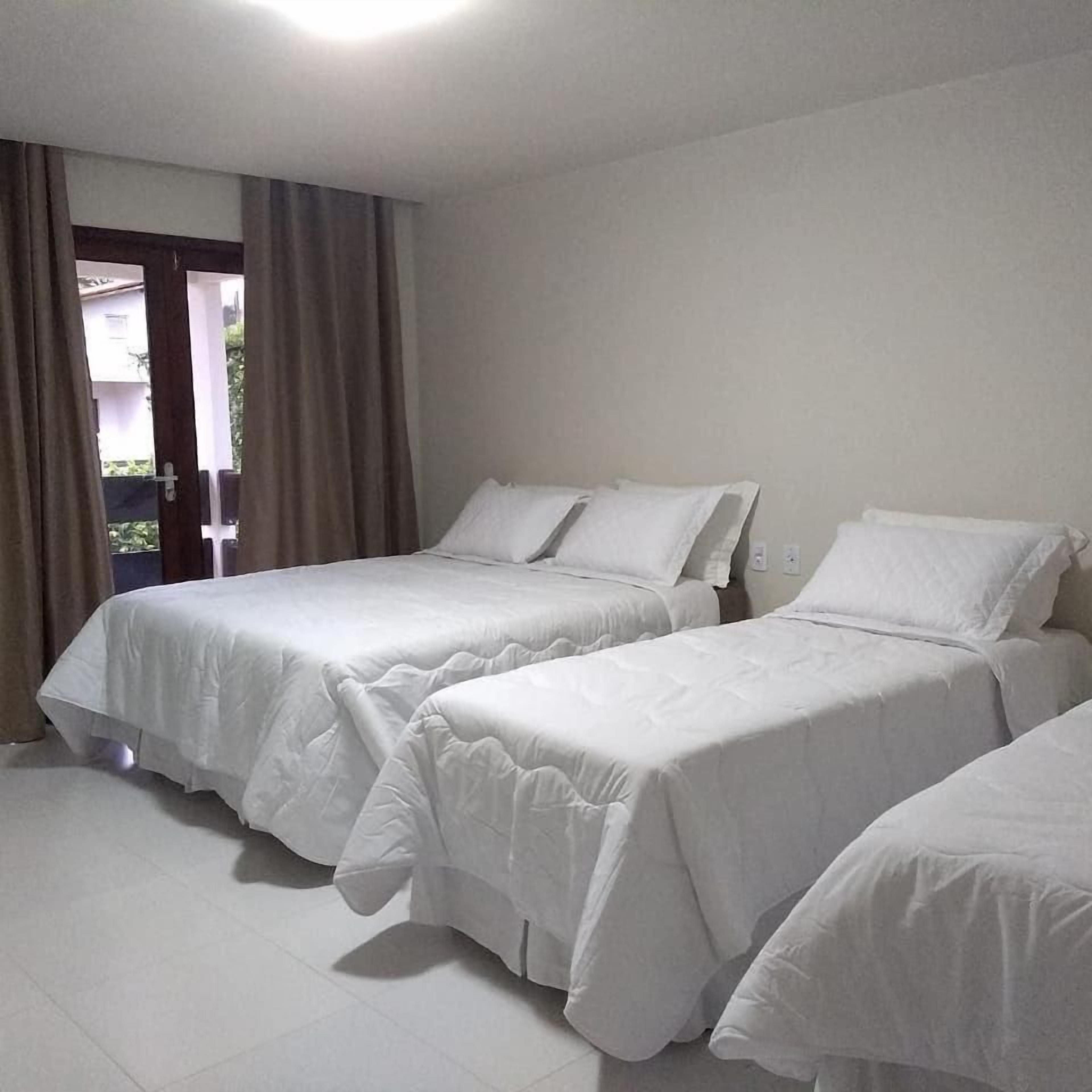 Una habitación de hotel con dos camas, una puerta que da a un balcón y un suelo de baldosas blancas.