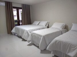 Habitación de hotel con tres camas individuales, una ventana con cortinas y suelo de baldosas.