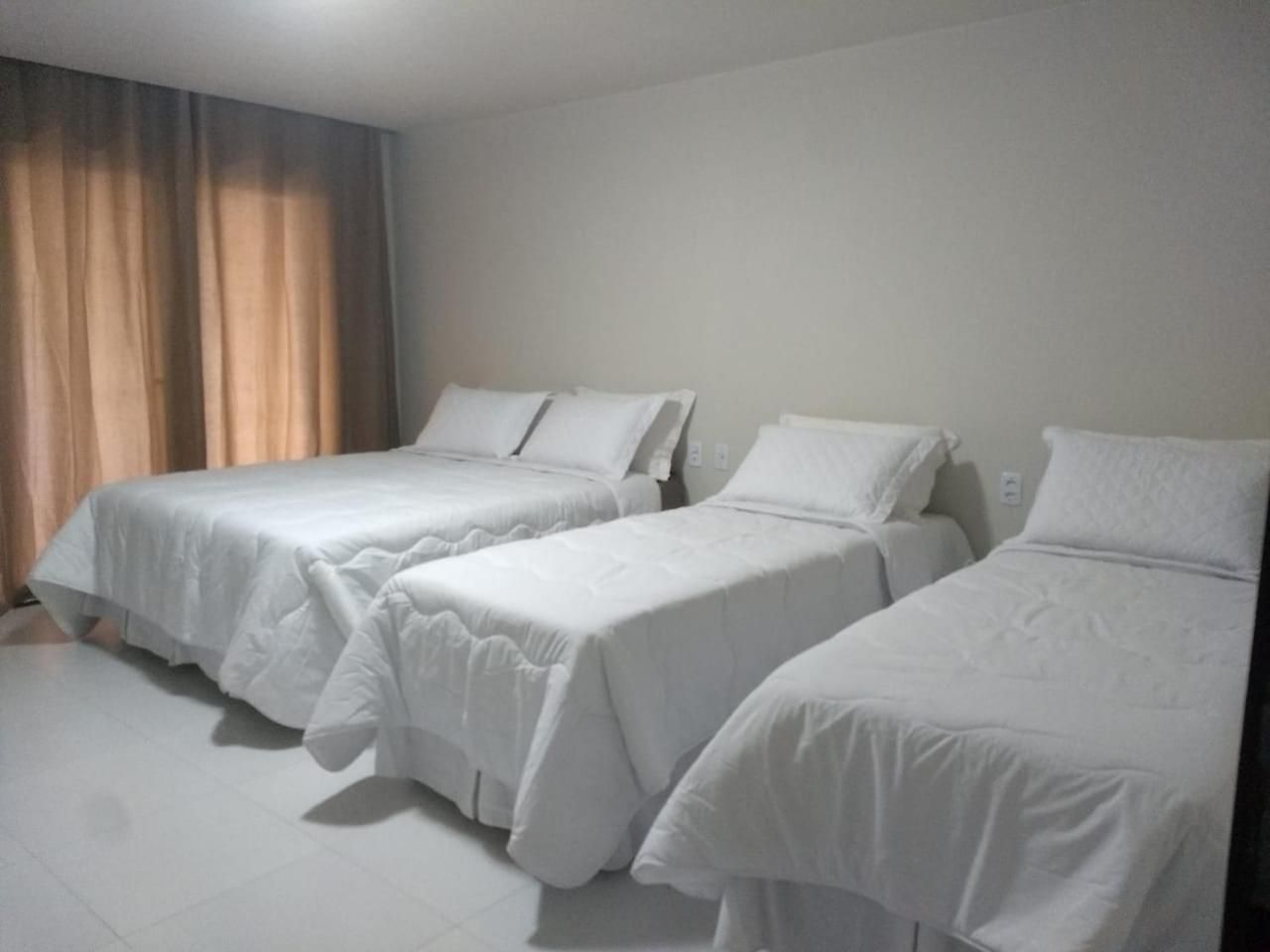 A hotel room with three single beds, a window with curtains, and a white floor.