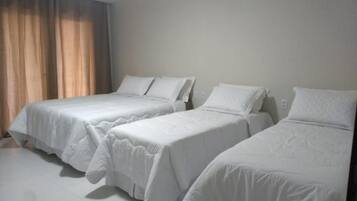 A hotel room with three single beds, a window with curtains, and a white floor.
