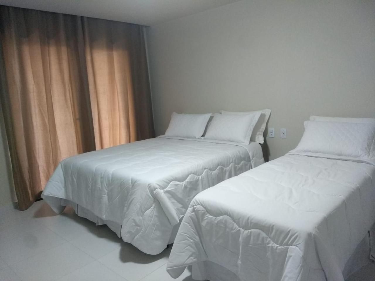 Une chambre d’hôtel avec deux lits simples, un rideau et un mur uni.