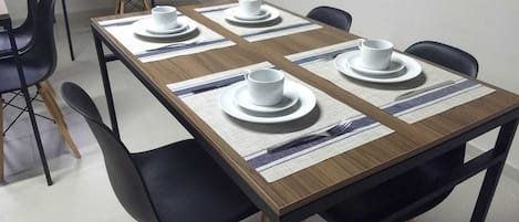 A dining area with a rectangular table set for four, surrounded by black chairs.