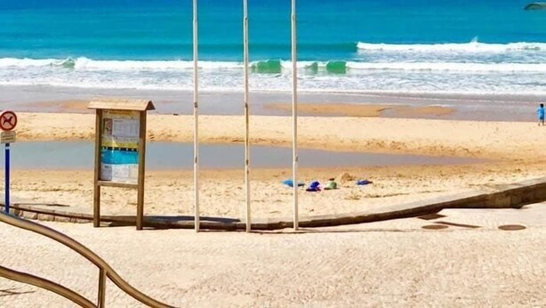 Ein Strand mit einem Rettungsturm, einem Verbotsschild zum Schwimmen und einer Person, die spazieren geht.