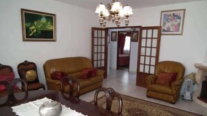 Ein Wohnzimmer mit Esstisch, zwei Ledersofas, einer Chandelüster und einer Tür zu einem anderen Raum.