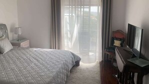 Ein Schlafzimmer mit einem Bett, einem Schreibtisch, einem Stuhl, einem Fernseher und einem Fenster mit Vorhängen.
