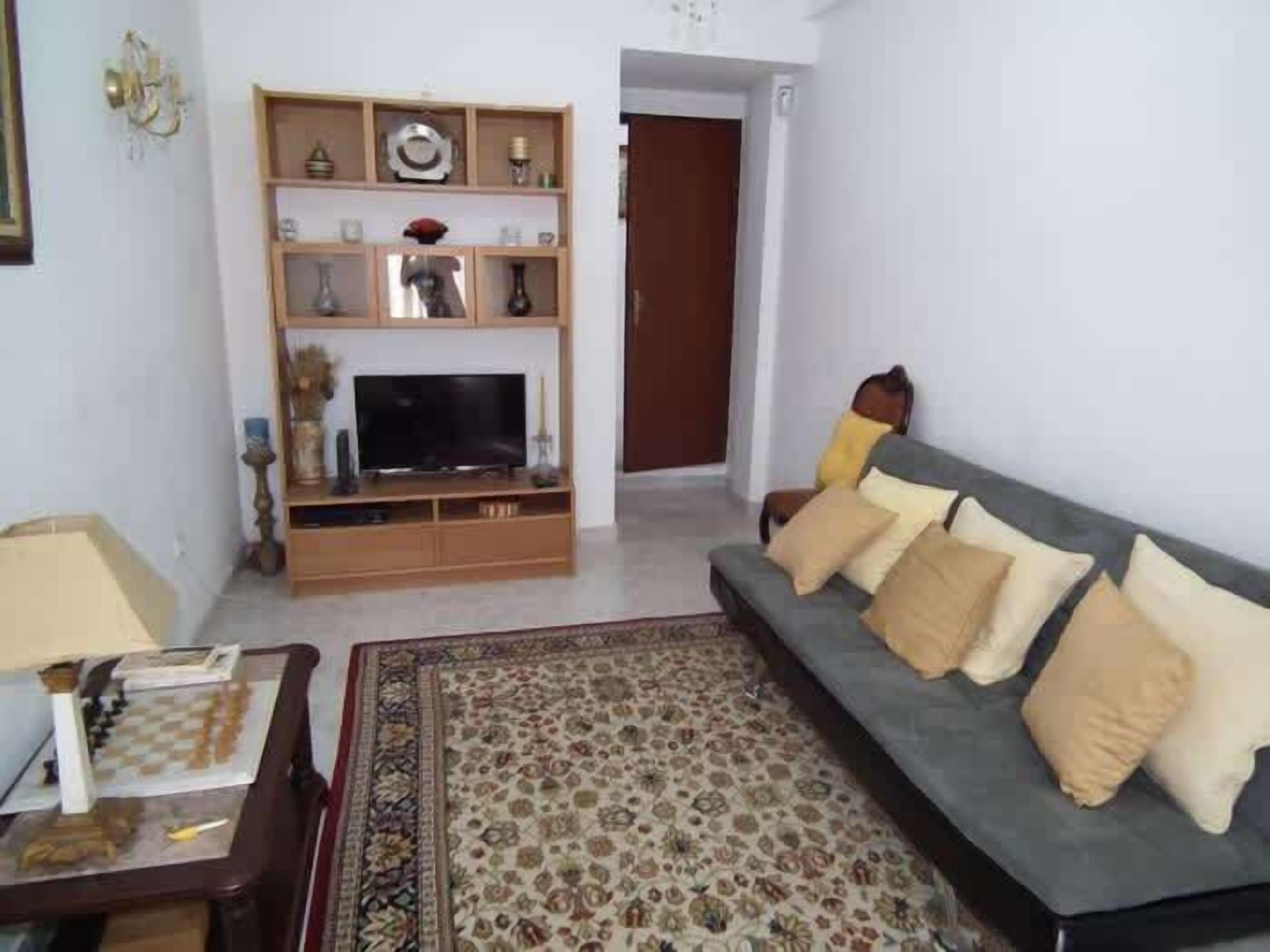 A living room with a television, a sofa, a patterned rug, and a wooden entertainment unit.