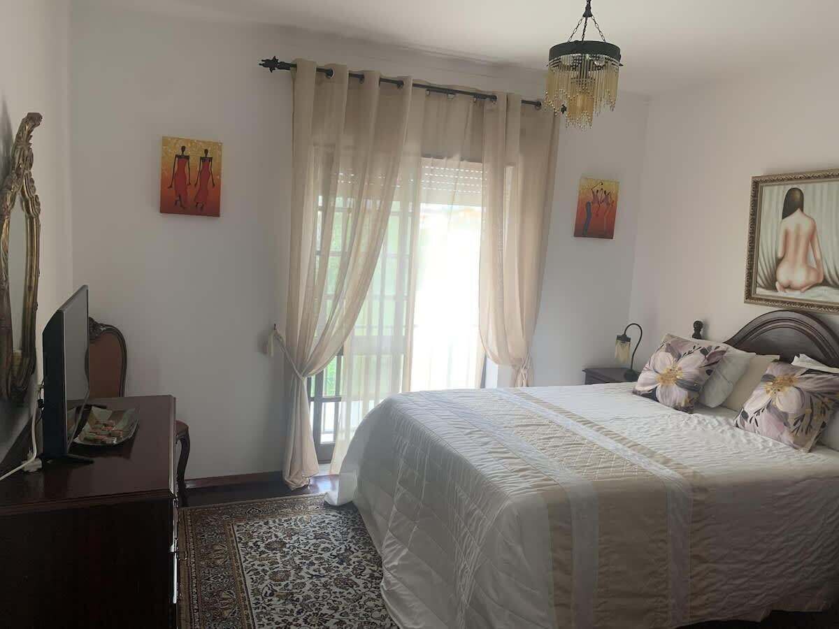 Ein Schlafzimmer mit Bett, Vorhängen, Schreibtisch, Stuhl und Bildern an den Wänden.