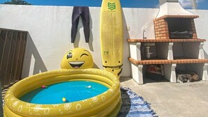 En uppblåsbar pool med ett leende ansikte, en surfbräda och en grill.