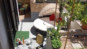Een terras met een ronde tafel en stoelen, omringd door potplanten en een auto op de achtergrond.