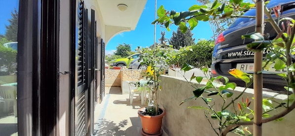 A balcony with potted plants, a stone wall, and a parked car.