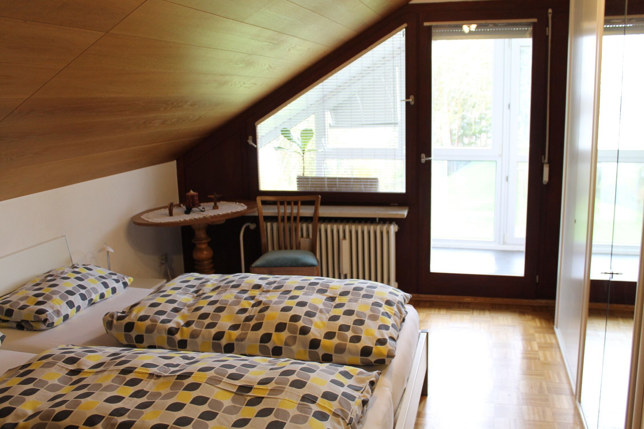 Quarto com duas camas, uma janela, um radiador e uma pequena mesa com cadeiras.