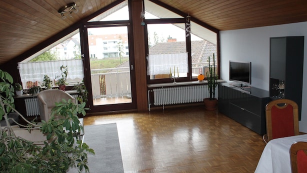 Une pièce spacieuse avec un plafond en pente, une télévision, un radiateur et une vue sur le balcon extérieur.