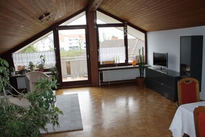Quarto espaçoso com teto inclinado, televisão, radiador e vista para a varanda externa.