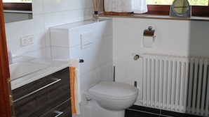 Une salle de bain avec des toilettes blanches, un lavabo et un espace douche.